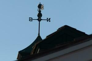 This weather vane was beautiful on the roof contrasted against the sky. The shadowy image with the clear blue sky in the background. The North, South, East, and West showing direction of the wind. photo