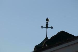 This weather vane was beautiful on the roof contrasted against the sky. The shadowy image with the clear blue sky in the background. The North, South, East, and West showing direction of the wind. photo