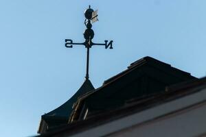 This weather vane was beautiful on the roof contrasted against the sky. The shadowy image with the clear blue sky in the background. The North, South, East, and West showing direction of the wind. photo