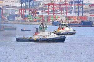 two tug boats in the water near a large container ship photo