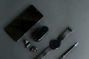 black pen, black smart watch, smartphone, wireless headphones on dark background photo