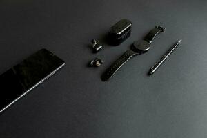 black pen, black smart watch, smartphone, wireless headphones on dark background photo