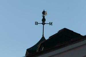 This weather vane was beautiful on the roof contrasted against the sky. The shadowy image with the clear blue sky in the background. The North, South, East, and West showing direction of the wind. photo