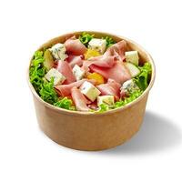 Paper bowl of salad with lettuce, blue cheese, prosciutto, pear, orange and mustard dressing isolated on white photo