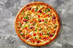 Colorful pizza with mozzarella, sous vide chicken, vegetable mix on gray stone surface photo