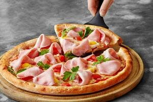 Female hand with serving spatula taking pizza with melted cheese, ham, quail eggs, tomatoes and greens photo