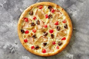 Pizza with smoked chicken, fried mushrooms, caramelized onions, tomatoes and cheese on gray surface photo