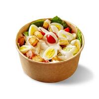 Caesar salad with lettuce, cherry tomatoes, quail eggs, croutons, chicken and sauce in cardboard bowl on white photo