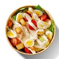 Top view of Caesar salad with lettuce, tomatoes, quail eggs, croutons, chicken and sauce in paper bowl isolated on white photo