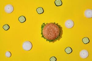 Tasty fresh unhealthy hamburger with ketchup and vegetables on yellow vibrant bright background. Top View with Copy Space. photo