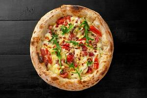 Boscaiola pizza with cream, mozzarella, cabanossi, salami, mushrooms, parmesan and fresh arugula on black wooden surface photo