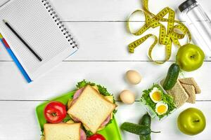 Healthy lunch in office at workplace or home. Whole-grain sandwich with ham and fresh vegetables and bottle of water. Top view, flat lay on wood photo