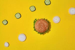 Tasty fresh unhealthy hamburger with ketchup and vegetables on yellow vibrant bright background. Top View with Copy Space. photo