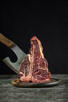 Fresh raw t-bones steak on an olive wooden board with sea salt and a kitchen ax. photo