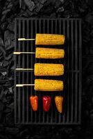 Grilled ears of corn and bell peppers on barbecue grate over cold coals photo