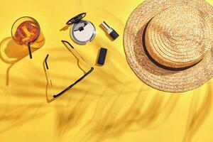 Straw beach woman's hat, beverage with ice in a glass and sun glasses on yellow background with shadow from a palm leaf. photo