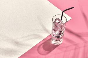 Glass of mineral water with ice on pink and white background with shadow from a palm leaf photo