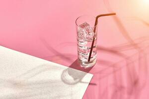 vaso de mineral agua con hielo en rosado y blanco antecedentes con sombra desde un palma hoja. Dom llamarada foto