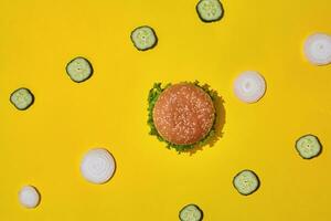 Tasty fresh unhealthy hamburger with ketchup and vegetables on yellow vibrant bright background. Top View with Copy Space. photo