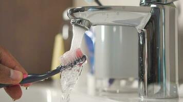 lento movimento do segurando escova de dente debaixo fluindo água dentro banheiro, fechar-se. video
