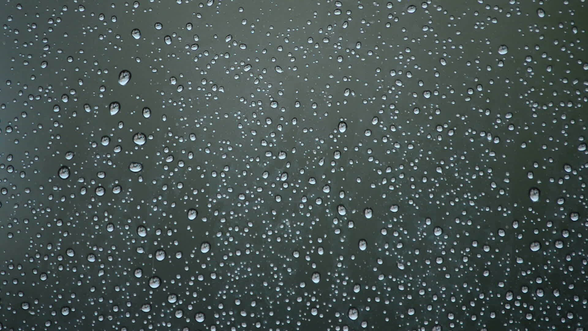 Raindrops sliding down the glass window of a room while it's raining