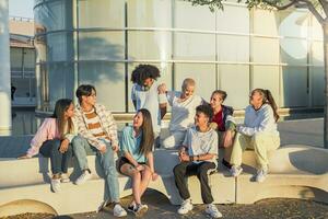 grande grupo de contento Adolescente amigos hablando en un banco en el calle de el estudiante instalaciones. foto