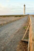 un de madera pasarela Guías a un faro en el playa foto