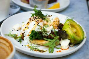 Poached egg on toast with avocado and herbs on a white plate photo