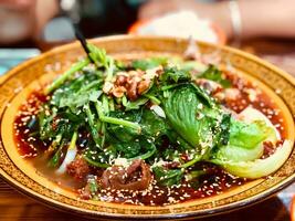 Spinach noodles with beef and vegetables in a bowl on tableSpinach noodles with beef and vegetables in a bowl on table photo