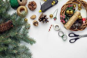 Preparing for Christmas or New Year holiday. Flat-lay of fur tree branches, wreaths, rope, scissors, craft paper over white table background, top view. photo