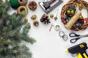 Preparing for Christmas or New Year holiday. Flat-lay of fur tree branches, wreaths, rope, scissors, craft paper over white table background, top view. photo