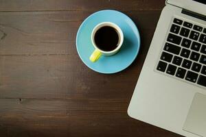 Coffee cup and laptop on wooden background. Top view. photo