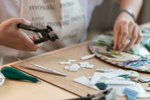 Workplace of the mosaic master women's hands holding tool for mosaic details in the process of making a mosaic photo