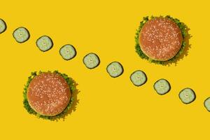 Two tasty fresh unhealthy hamburgers with ketchup and vegetables on yellow vibrant bright background. Top View with Copy Space. photo