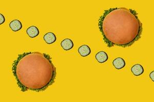 Two tasty fresh unhealthy hamburgers with ketchup and vegetables on yellow vibrant bright background. Top View with Copy Space. photo