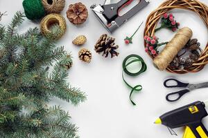 Preparing for Christmas or New Year holiday. Flat-lay of fur tree branches, wreaths, rope, scissors, craft paper over white table background, top view. photo