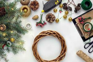 Preparing for Christmas or New Year holiday. Flat-lay of fur tree branches, wreaths, rope, scissors, craft paper over white table background, top view. photo