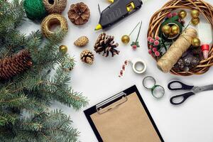 Preparing for Christmas or New Year holiday. Flat-lay of fur tree branches, wreaths, rope, scissors, craft paper over white table background, top view. photo