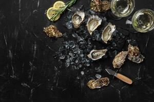 Fresh opened oysters, ice, lemon on a rectangle slate and champagne are on a black stone textured background. Top view with copy space. Close-up. photo