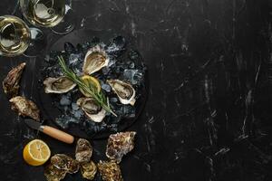 Fresh opened oysters, ice, lemon on a round slate and champagne are on a black stone textured background. Top view with copy space. Close-up. photo