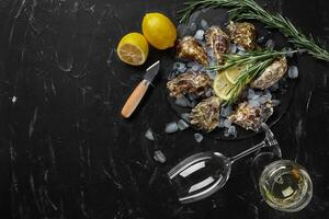 Fresh closed oysters, ice, lemon on a round slate and champagne are on a black stone textured background. Top view with copy space. Close-up shot. photo