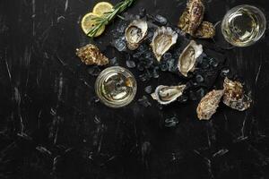 Fresh opened oysters, ice, lemon on a rectangle slate and champagne are on a black stone textured background. Top view with copy space. Close-up. photo