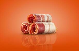 Palatable slices of a rolled bacon on an orange background with copy space for text or images, mirror surface. Advertising concept. Close-up shot. photo