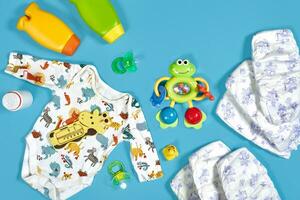 Baby care with bath set. Nipple, toy, clothes, shampoo on blue background top view mockup photo