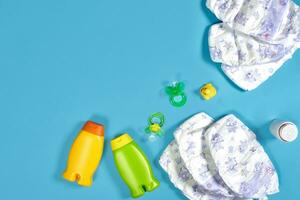 Baby care with bath set. Nipple, toy, diapers, shampoo on blue background top view mockup photo