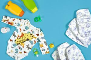 Baby care with bath set. Nipple, toy, clothes, shampoo on blue background top view mockup photo