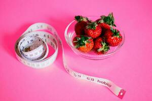 Strawberries and measuring tape on pink background. Healthy eating concept. photo