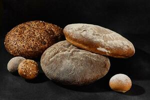 Assortment of tasty baked round bread and buns with sesame and sunflower seeds, sprinkled with flour. Black background, copy space. Close-up photo