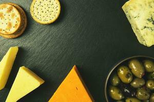 Different types of cheese with olives and crackers on black background photo