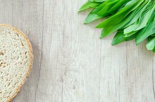 Wild garlic leaves and bread on wooden background, top view, copy space photo